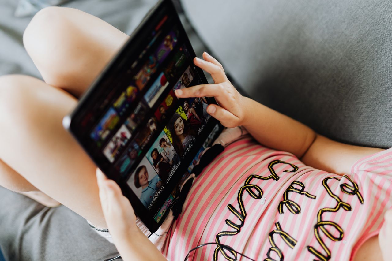 Young girl lying down using a tablet for entertainment and learning indoors.
